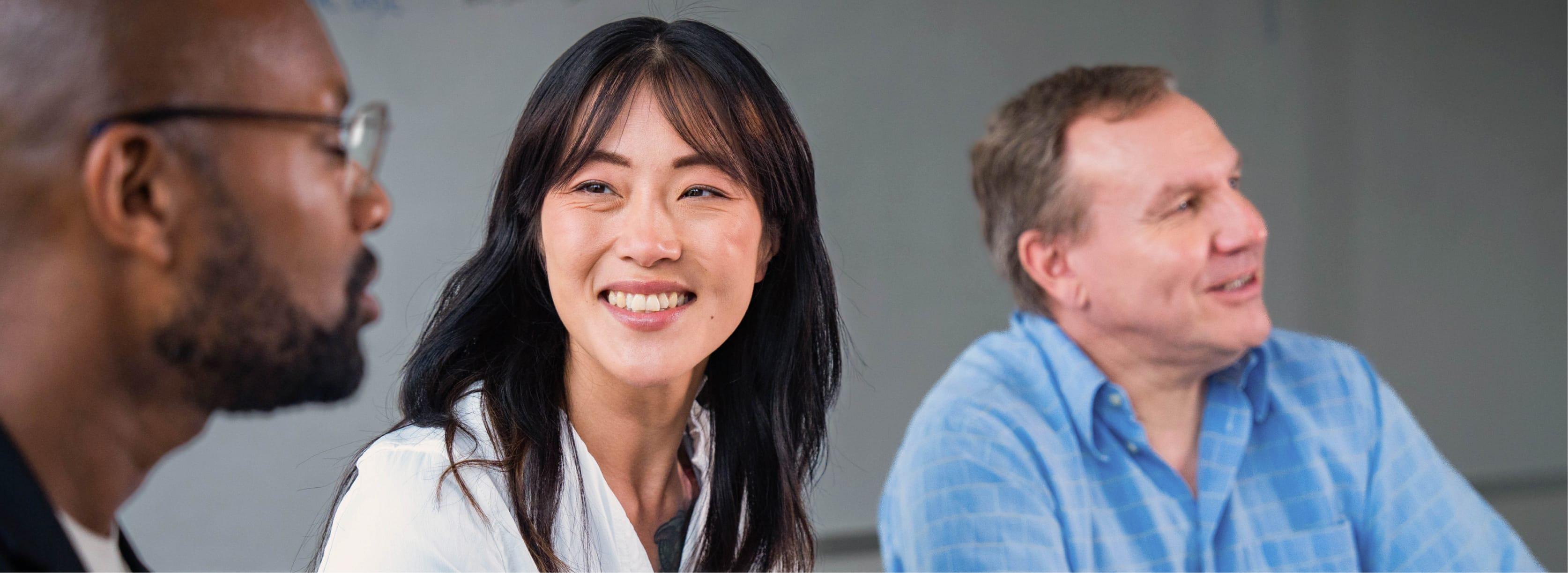 Three multicultural people in an office smiling.