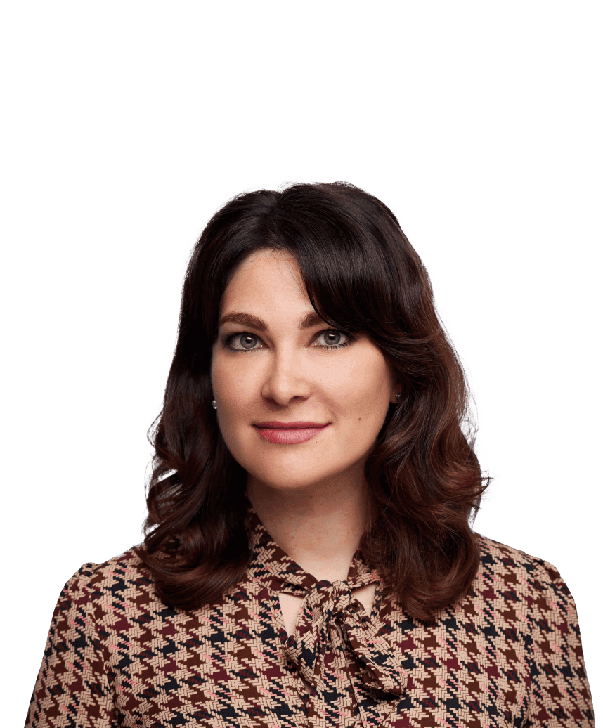 A brunette woman in a brown houndstooth patterned shirt is standing in front of a blurred background. She looks into the camera with a closed-mouth smile.
