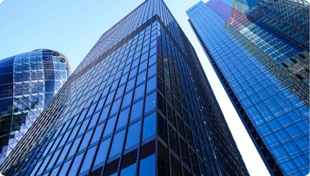 An upwards angle of skyscrapers in the city of London, with the Gherkin building in the back of the frame.