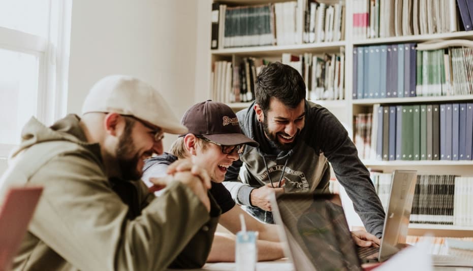 Three people excited and smiling looking at a laptop screen in a library setting