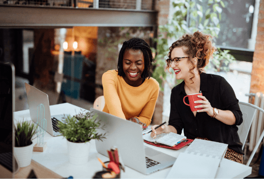 Two smiling women collaborating at their desk